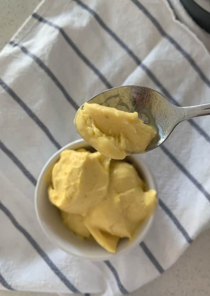 Helado de mango en un recipiente con una cuchara encima de un paño de cocina rayado 