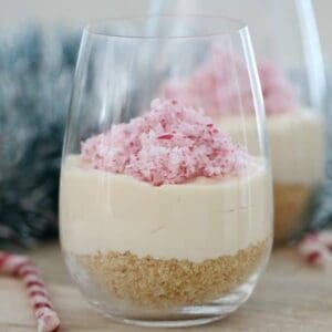 Un vaso alto con base de galleta, tarta de queso y bastón de caramelo picado encima.