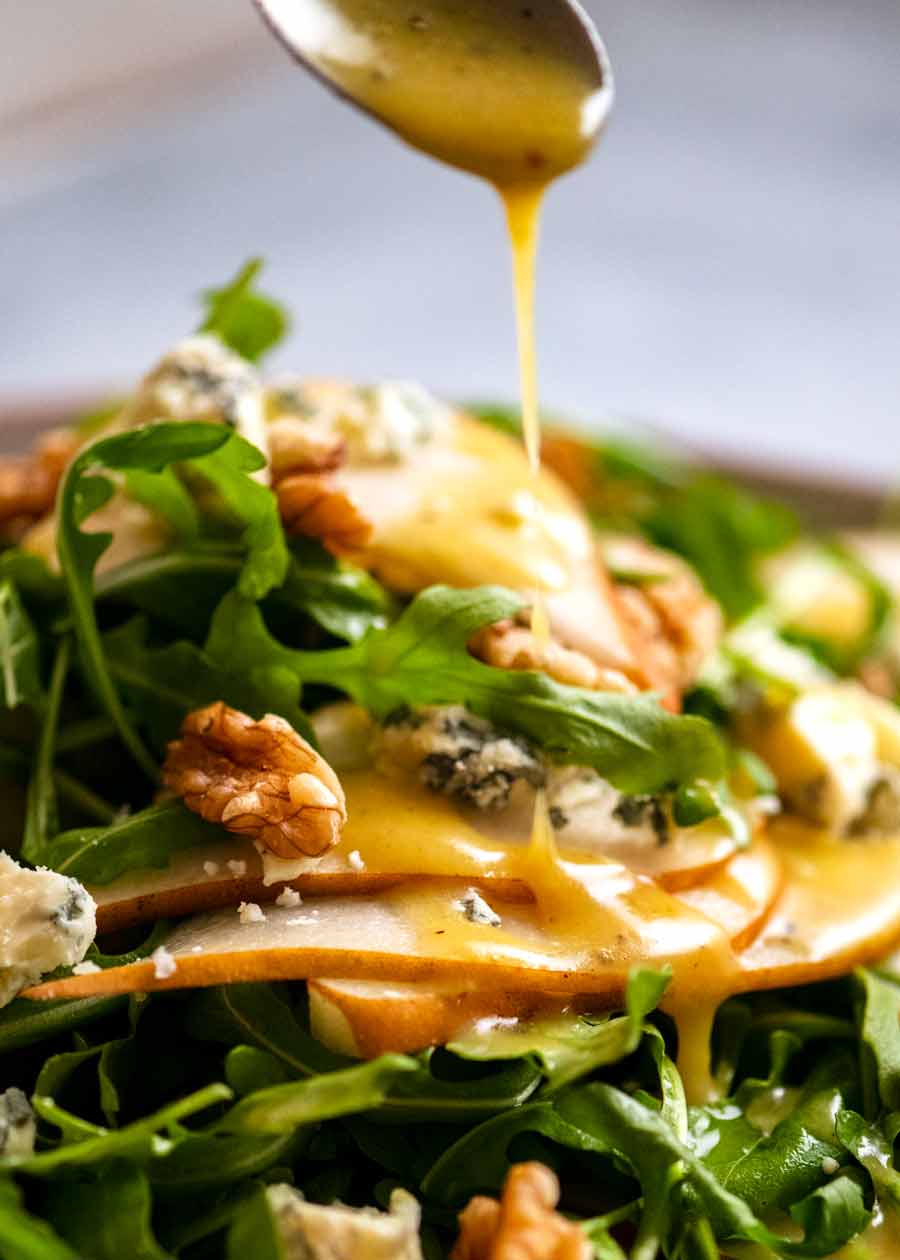 Rociar aderezo de mostaza y miel sobre ensalada de peras con queso azul y rúcula