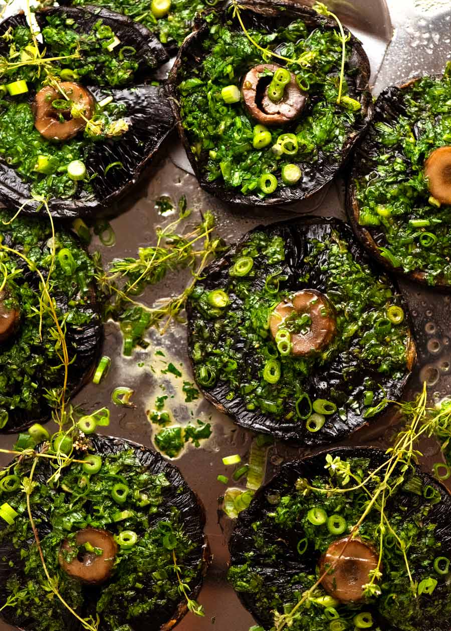 Fotografía aérea de champiñones grandes asados ​​con mantequilla de tomillo de cebolla verde en una bandeja, listos para ser servidos