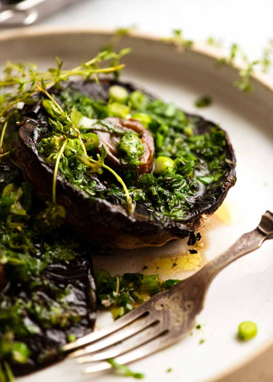Champiñones grandes asados ​​con mantequilla de tomillo de cebolla verde en un plato, listos para comer