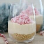 Un vaso alto con base de galleta, tarta de queso y bastón de caramelo picado encima.