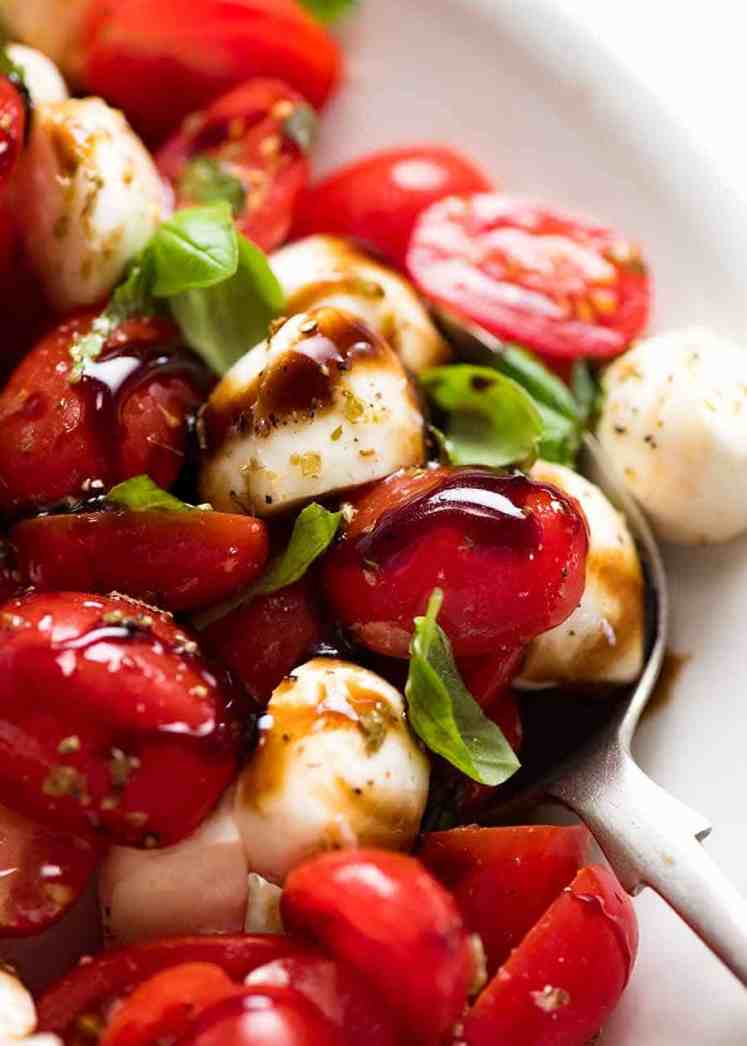 Cierre de ensalada Caprese con tomates cherry, mozzarella baby / bocconcini, hojas de albahaca y aderezo para ensalada Caprese con ajo y hierbas y rociado con glaseado balsámico.