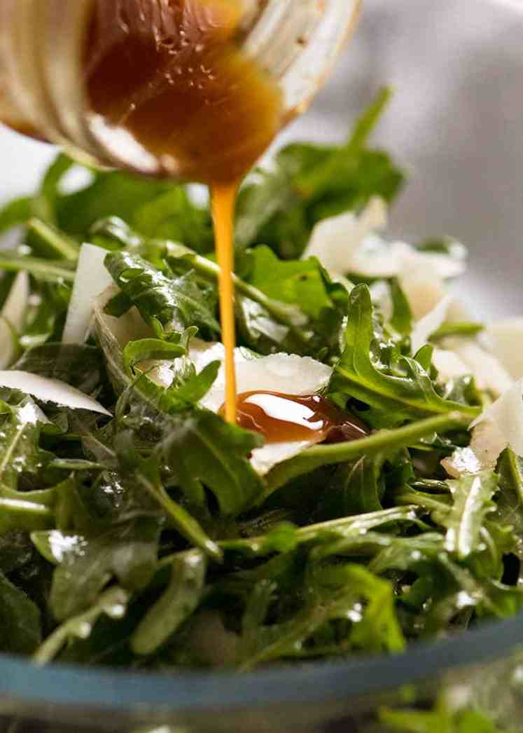 Cerca de aderezo balsámico se rocía sobre ensalada de rúcula con parmesano afeitado