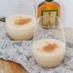 Dos vasos, medio llenos con una bebida de ponche de huevo lechoso espolvoreado con nuez moscada, y una pequeña botella de brandy en el fondo