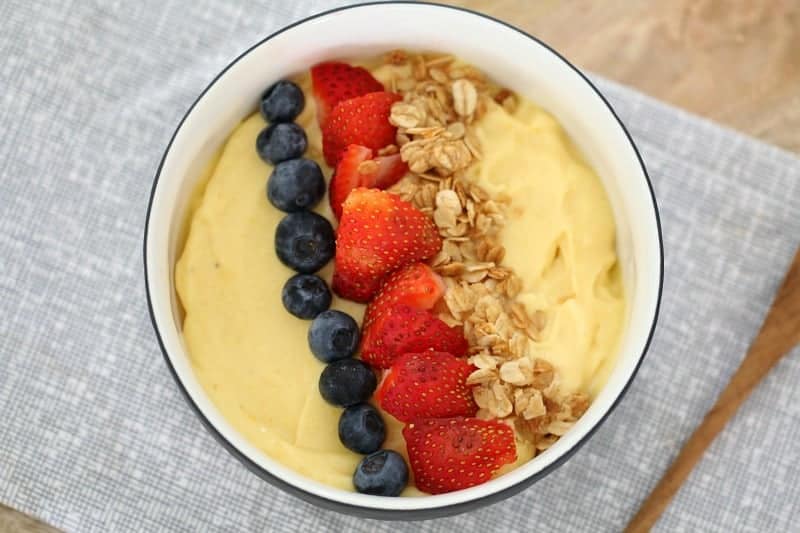 Un bol con batido de mango con arándanos, fresas y muesli encima.