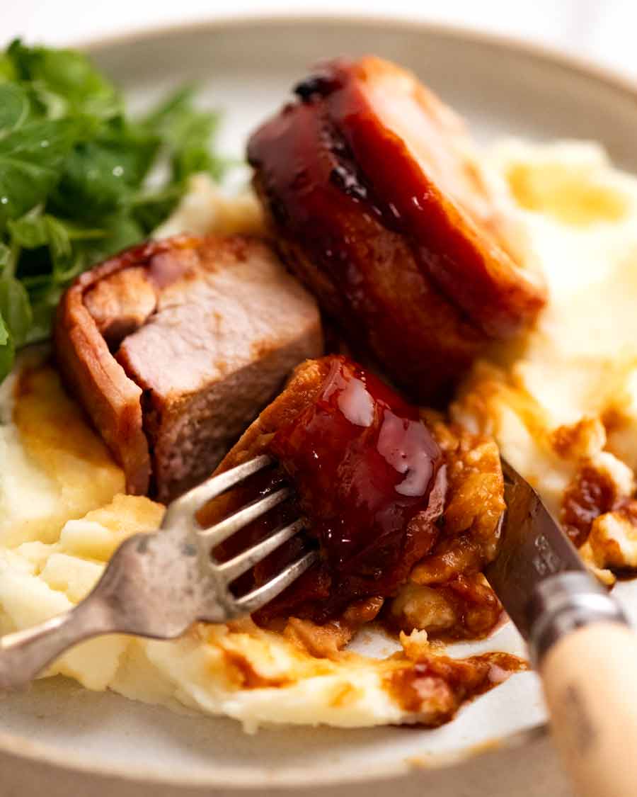 Rebanadas de lomo de cerdo envuelto en tocino sobre puré de papa