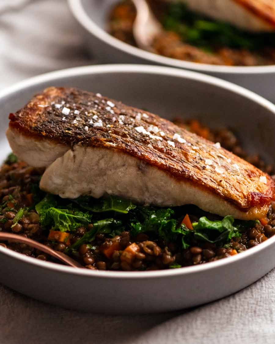 Barramundi de piel crujiente servido con una guarnición de ragu de lentejas francesas