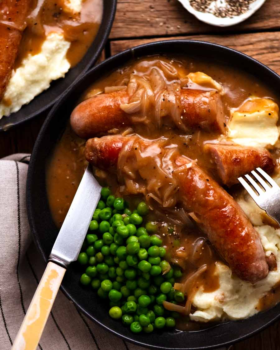 Salchichas y puré (salchicha con salsa de cebolla) en un plato con puré de patatas y guisantes