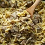 Una porción de stroganoff con fideos de huevo que se saca de una olla de cocción lenta con una cuchara de madera.
