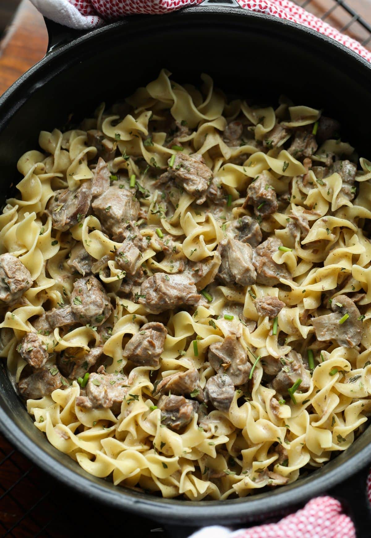 Fotografía cenital de una olla de barro de cerámica oscura y redonda llena de fideos de huevo y trozos de carne de res en una cremosa salsa stroganoff.