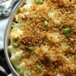 Una foto de una cazuela de coliflor horneada cubierta con pan rallado y adornada con cebolla verde.