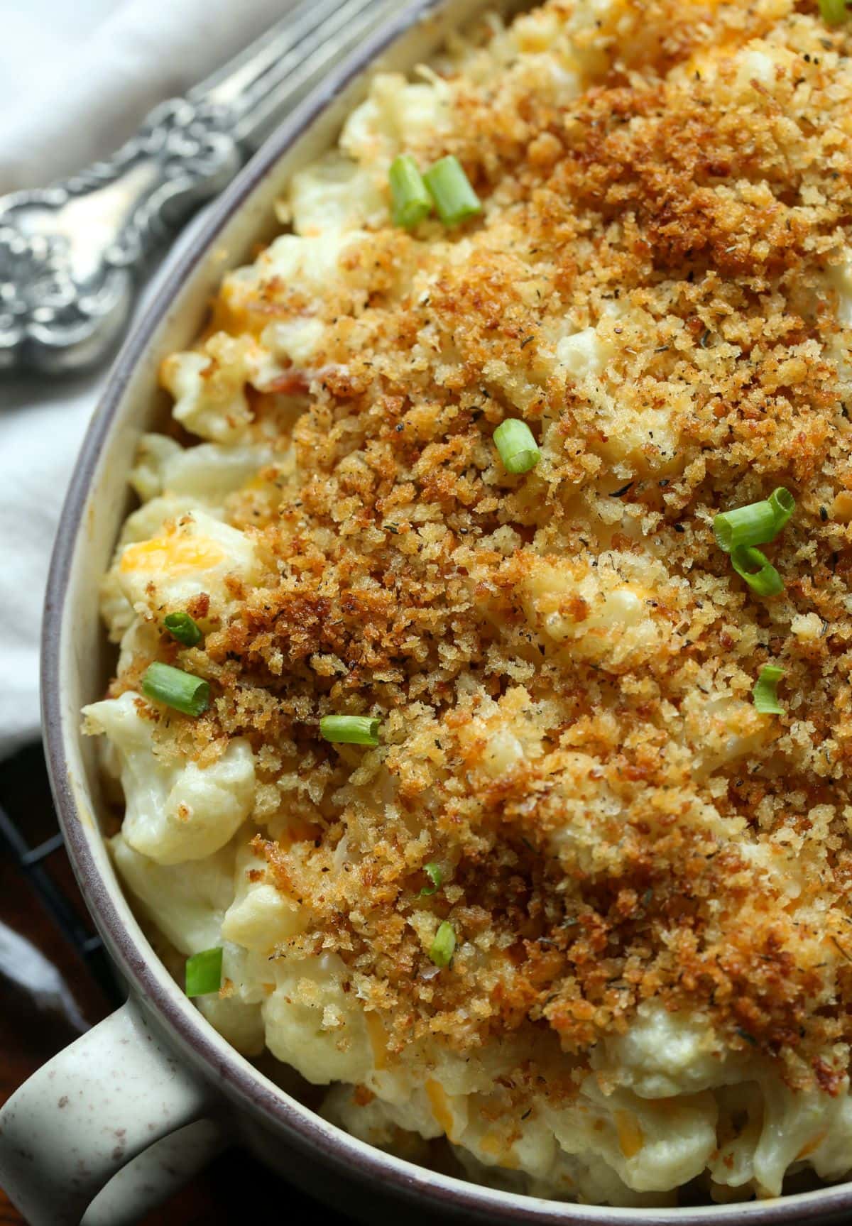 Una foto de una cazuela de coliflor horneada cubierta con pan rallado y adornada con cebolla verde.