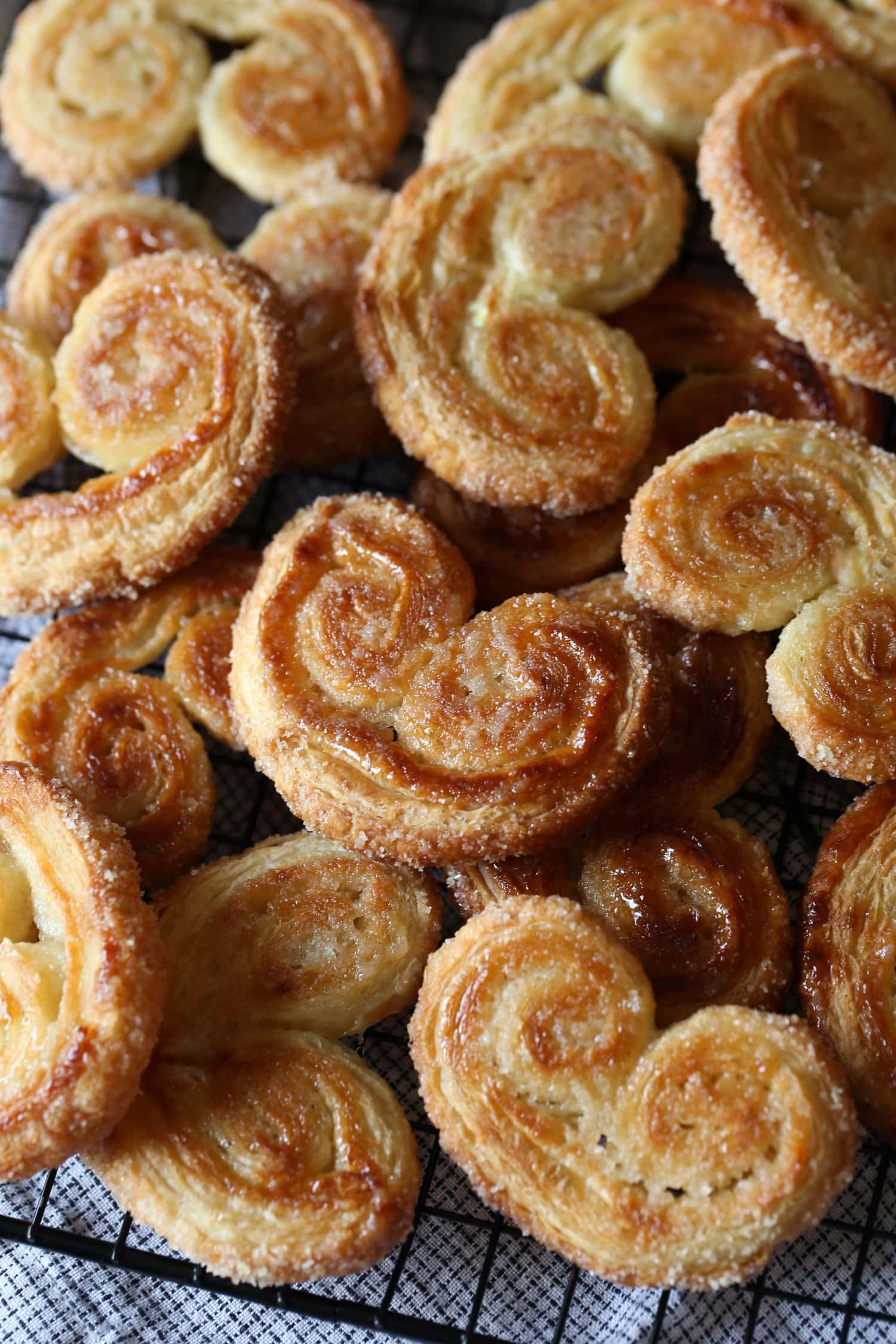 Un surtido de crujientes y doradas galletas palmier apiladas sobre una rejilla de alambre.