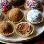 Bolas de ron navideñas decoradas en tazas de caramelo, dispuestas en un plato, a uno le falta un bocado.