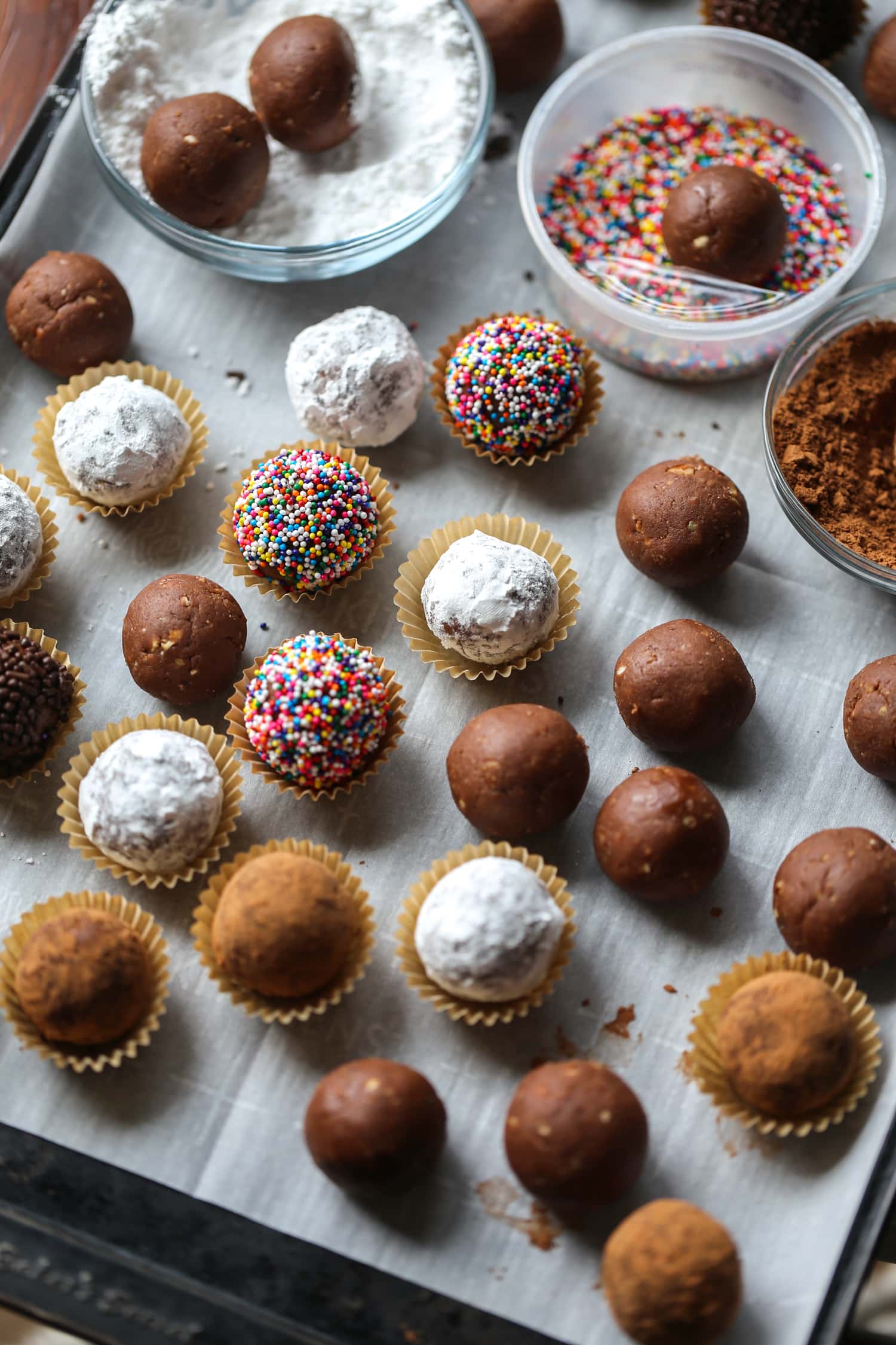 Bolas de ron navideñas decoradas con chispas, cacao y azúcar en polvo, colocadas en tazas de caramelo.