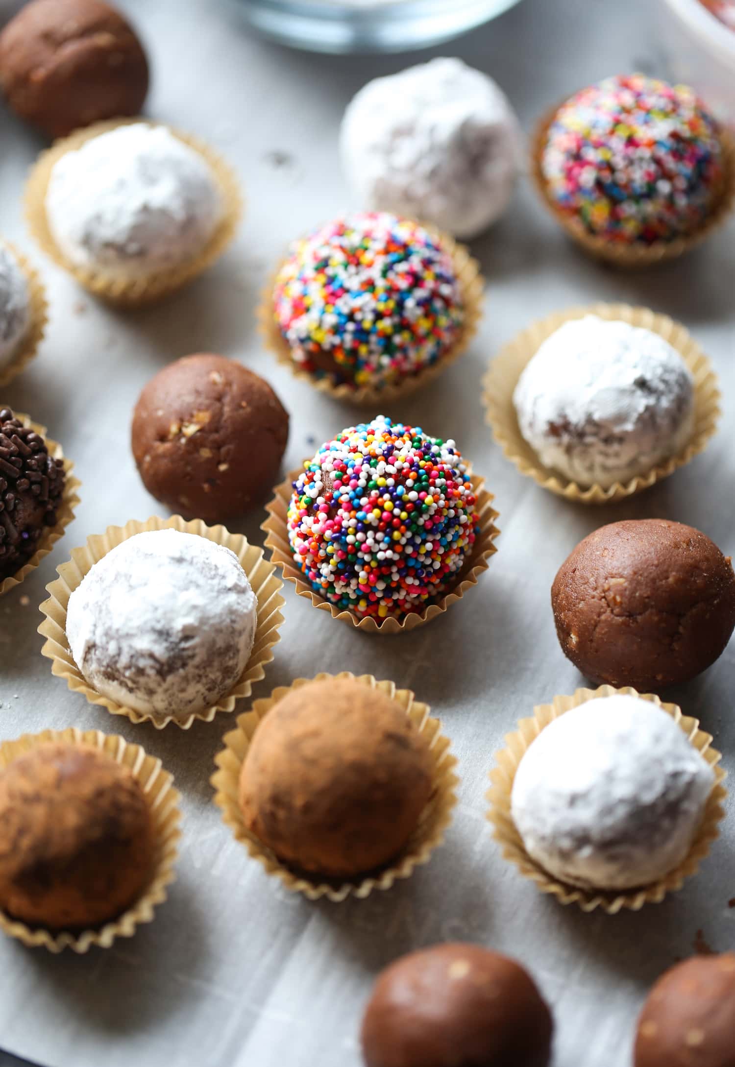 Bolas de ron navideñas decoradas con chispas, cacao y azúcar en polvo, colocadas en tazas de caramelo.