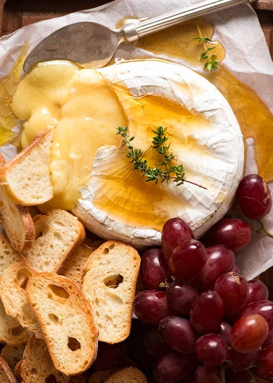 Fotografía aérea de Brie horneado rociado con miel, servido con pan tostado crujiente y uvas.