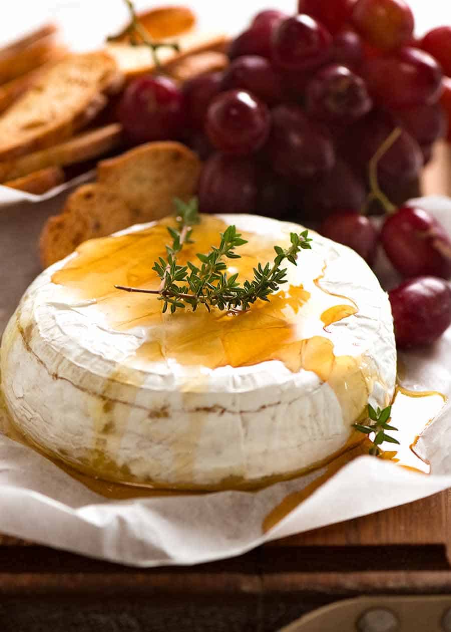 Foto de queso brie al horno rociado con miel aderezado con tomillo fresco, con pan tostado crujiente y uvas