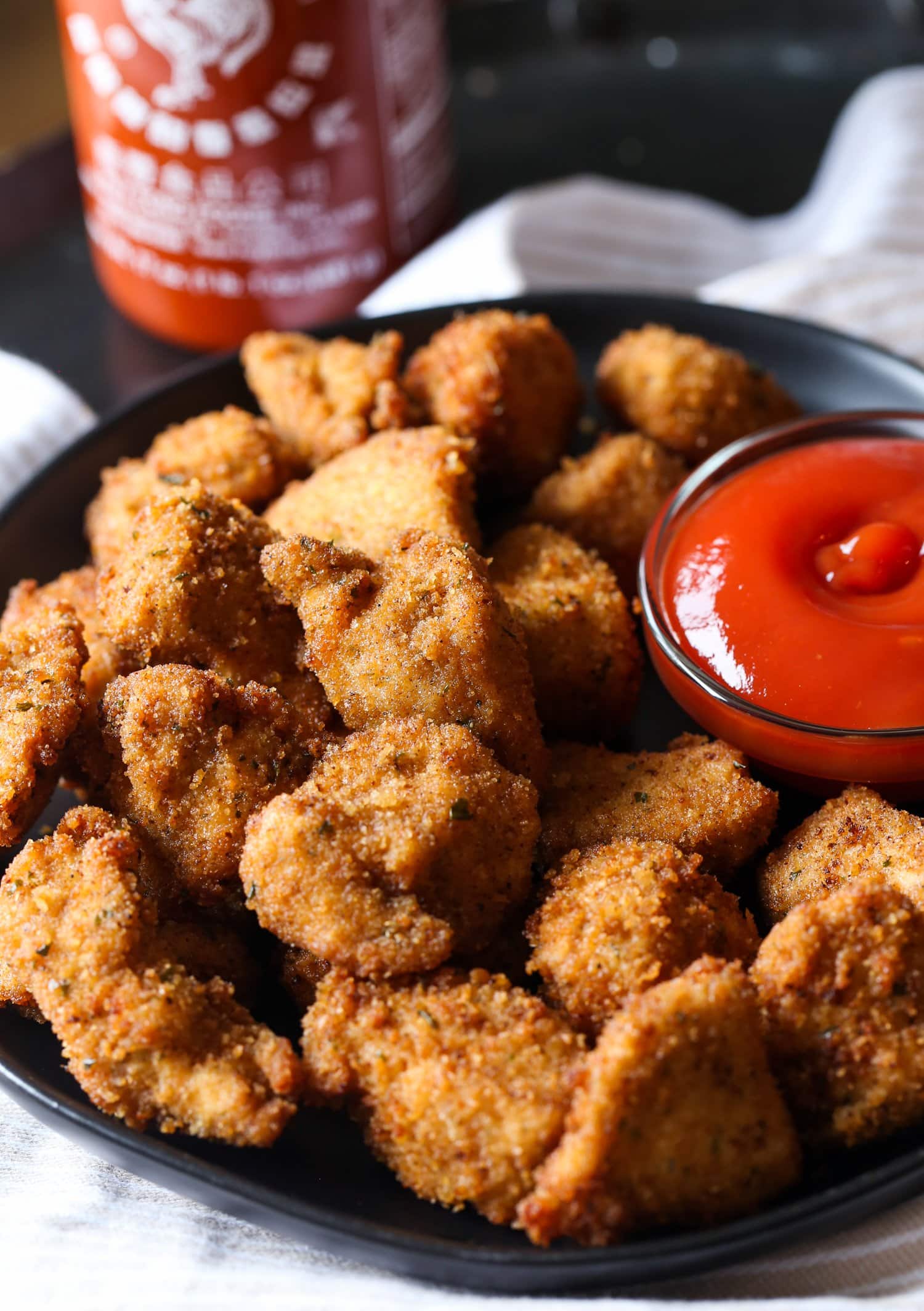 Nuggets de pollo caseros picantes en un plato junto a la salsa para mojar.