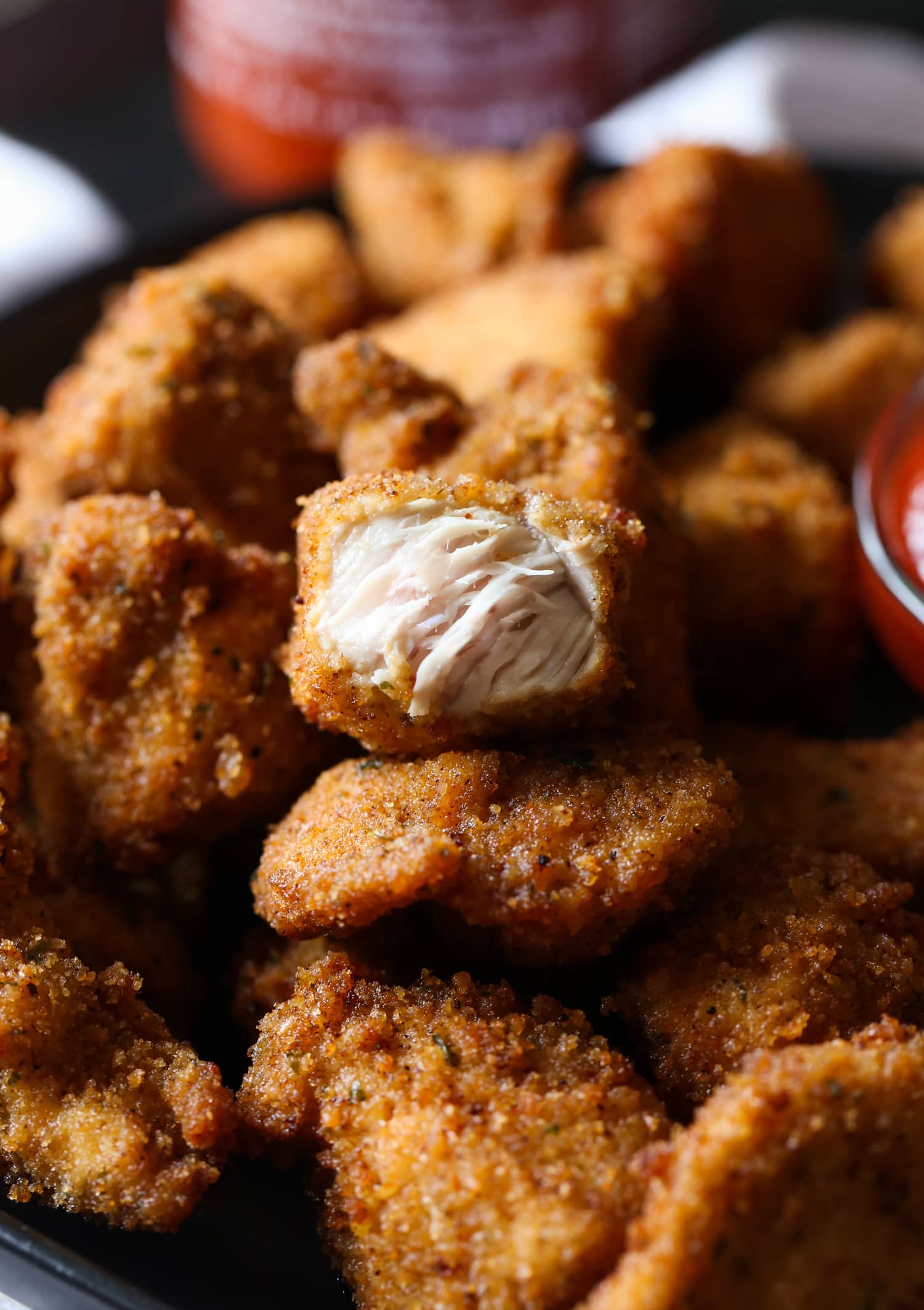 Un plato lleno de nuggets picantes caseros, con un nugget de pollo abierto para revelar el interior tierno y jugoso.