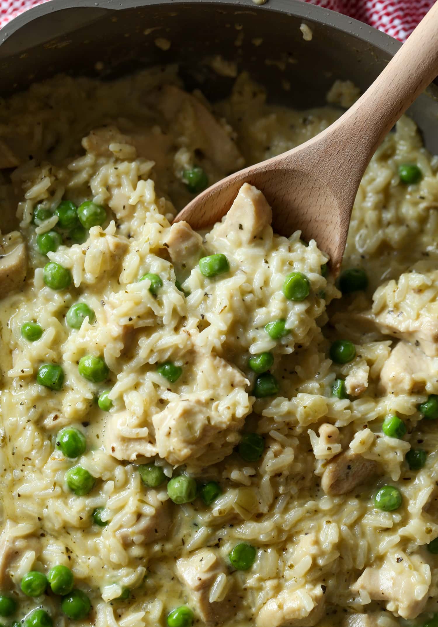 Se usa una cuchara de madera para servir pollo cremoso y arroz con guisantes verdes.