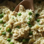 Se usa una cuchara de madera para servir pollo cremoso y arroz con guisantes verdes.