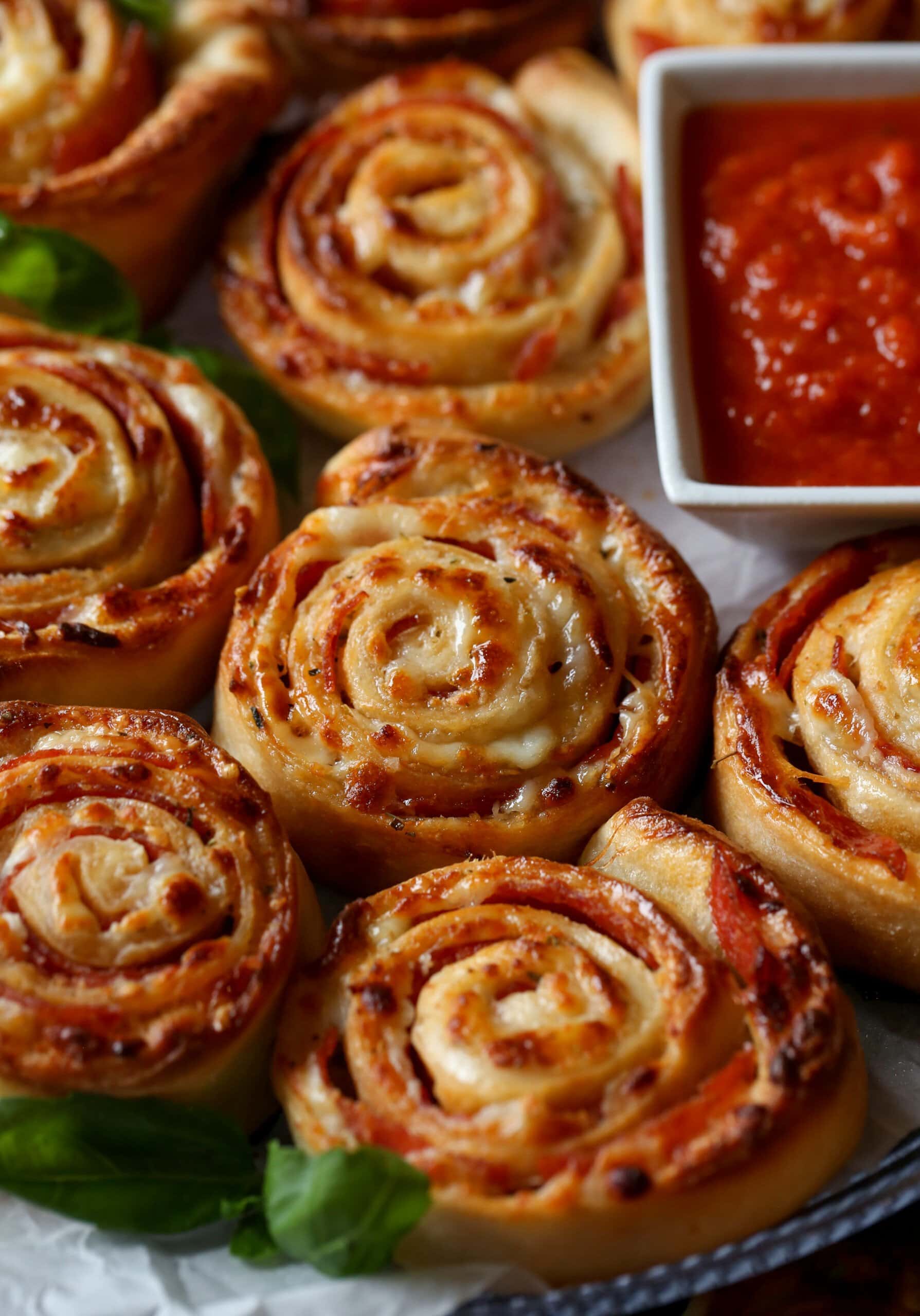 Rollos de pizza caseros junto a un tazón de salsa de pizza para mojar.