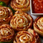 Rollos de pizza caseros junto a un tazón de salsa de pizza para mojar.