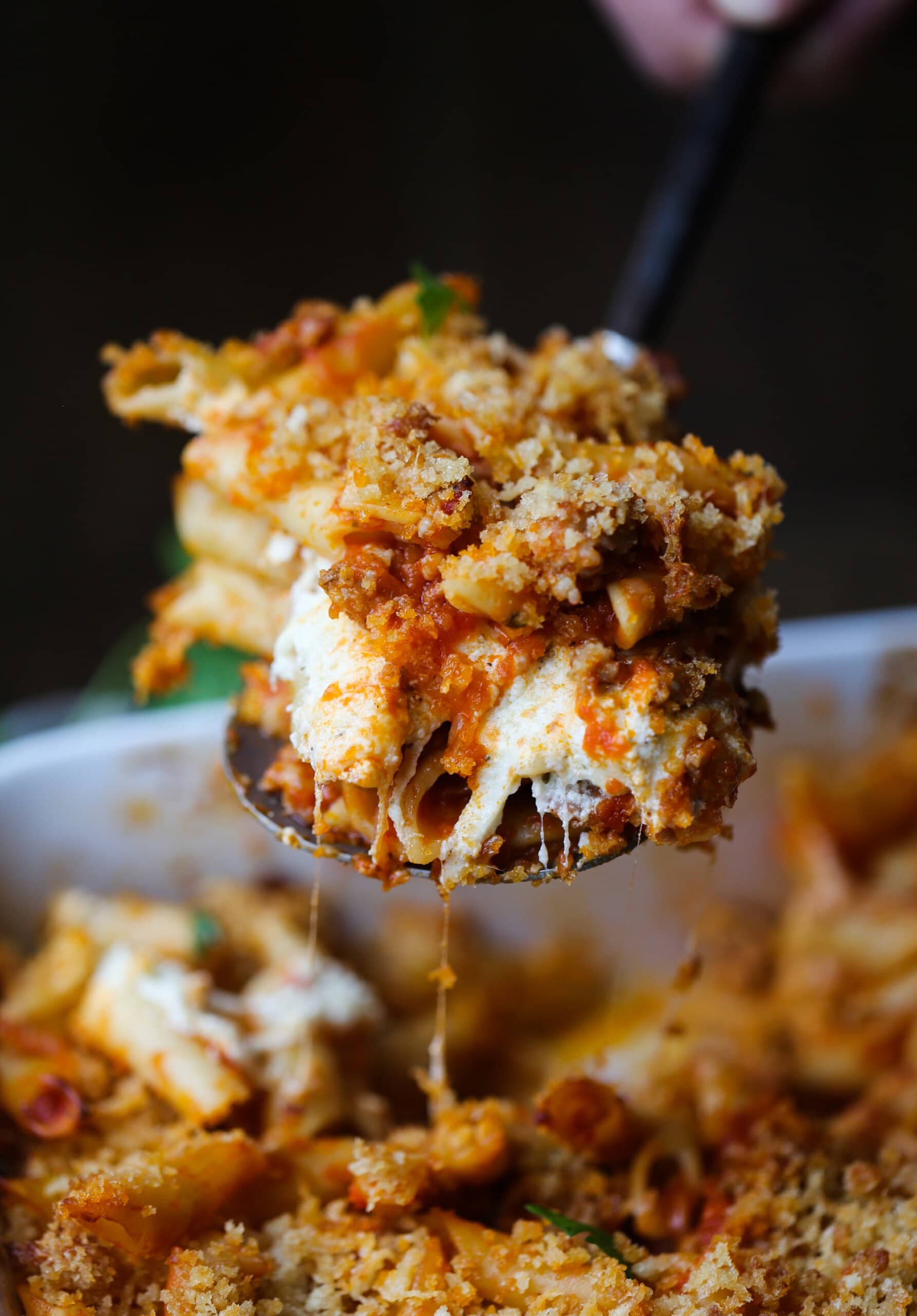 Una cucharada de mostaccioli horneado con queso se sirve en una cacerola.
