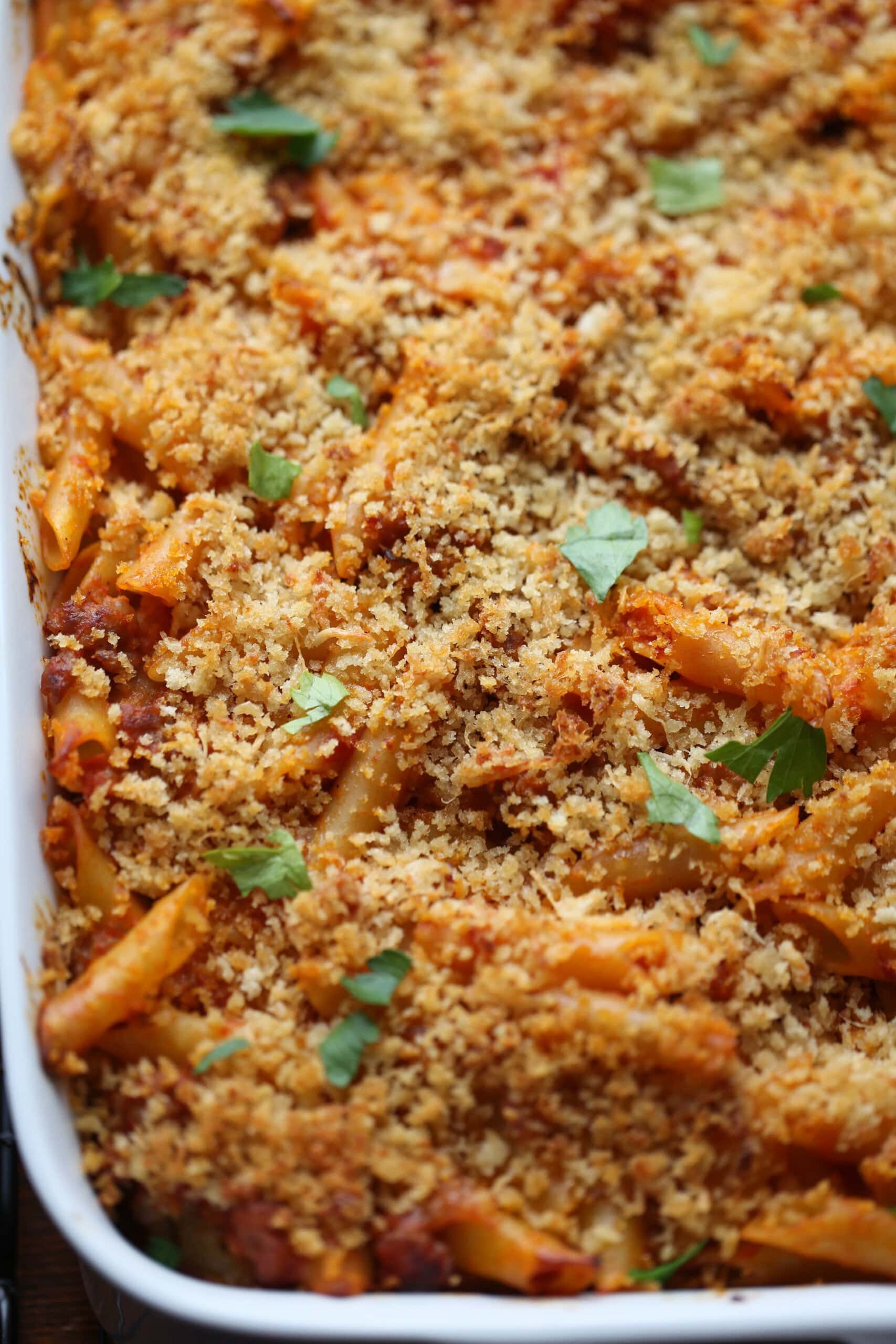 Primer plano de mostaccioli horneado cubierto con queso parmesano y pan rallado.