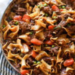 Carne de res y fideos cocinados en un plato con zanahorias y guisantes