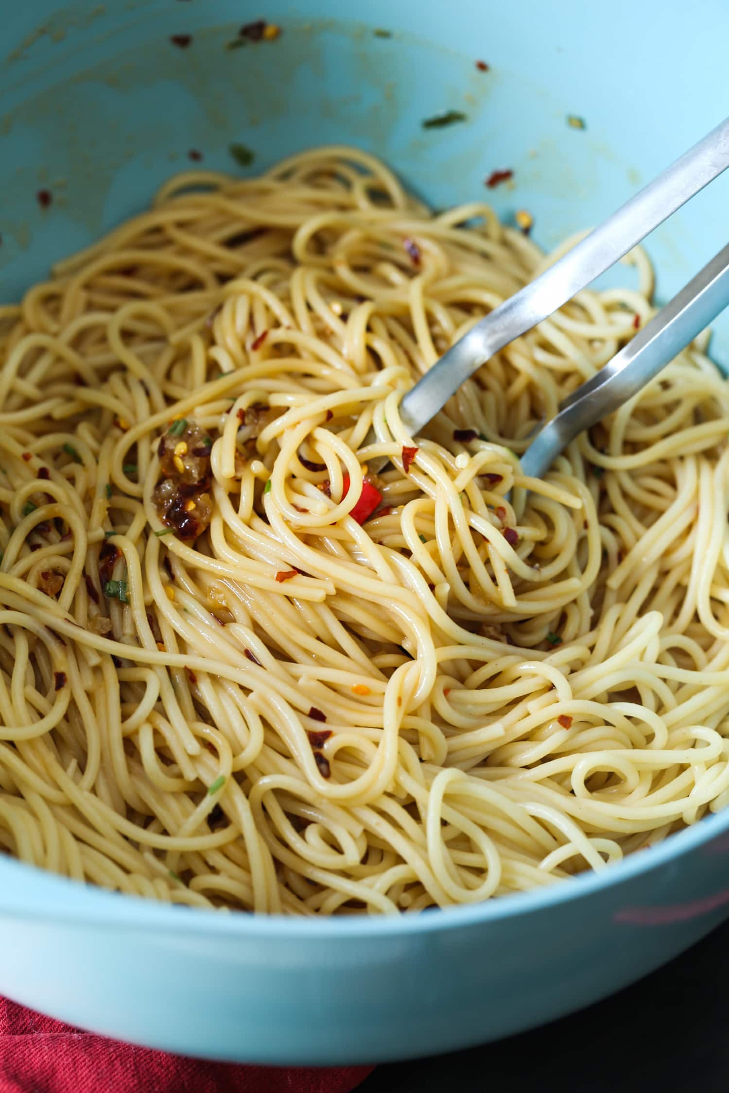 Las pinzas se usan para mezclar linguini con salsa picante de maní y sésamo.