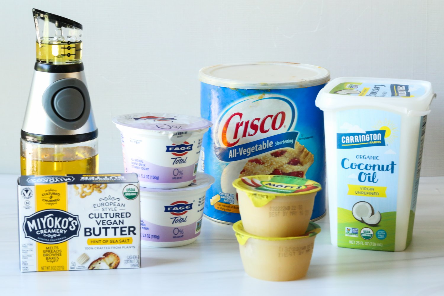 aceite de oliva, mantequilla vegana, compota de manzana, manteca vegetal, yogur griego y aceite de coco en un mostrador