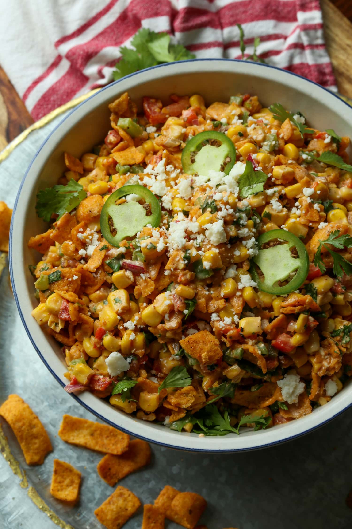 Ensalada picante de maíz Frito cubierta con queso cotija y jalapeños rebanados en una ensaladera blanca grande.