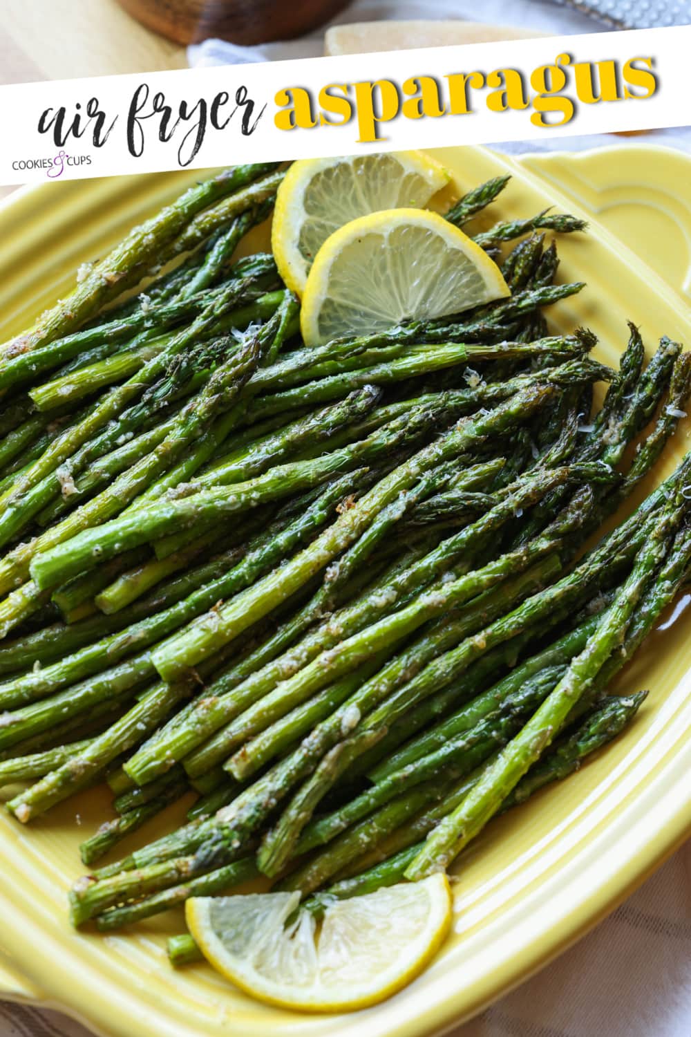 Espárragos asados ​​en una freidora en un plato de servir cuadrado amarillo, adornados con rodajas de limón.