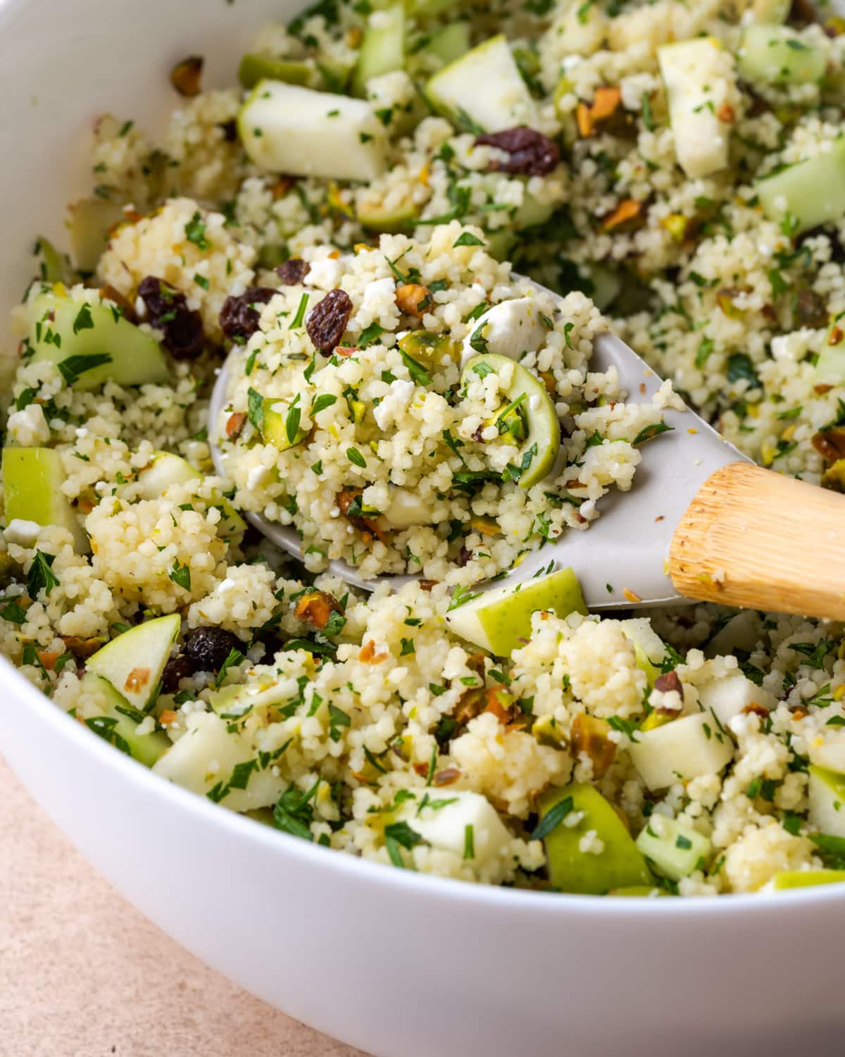 Ensalada mediterránea de cuscús en un tazón blanco grande con una cuchara de madera.
