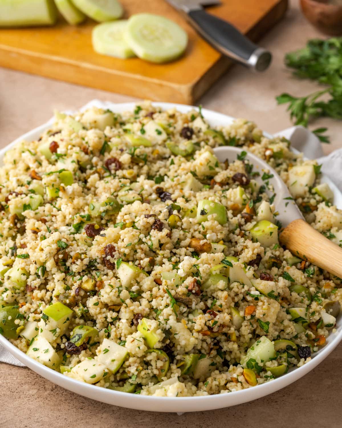 Ensalada mediterránea de cuscús en un plato blanco grande con una cuchara de madera.