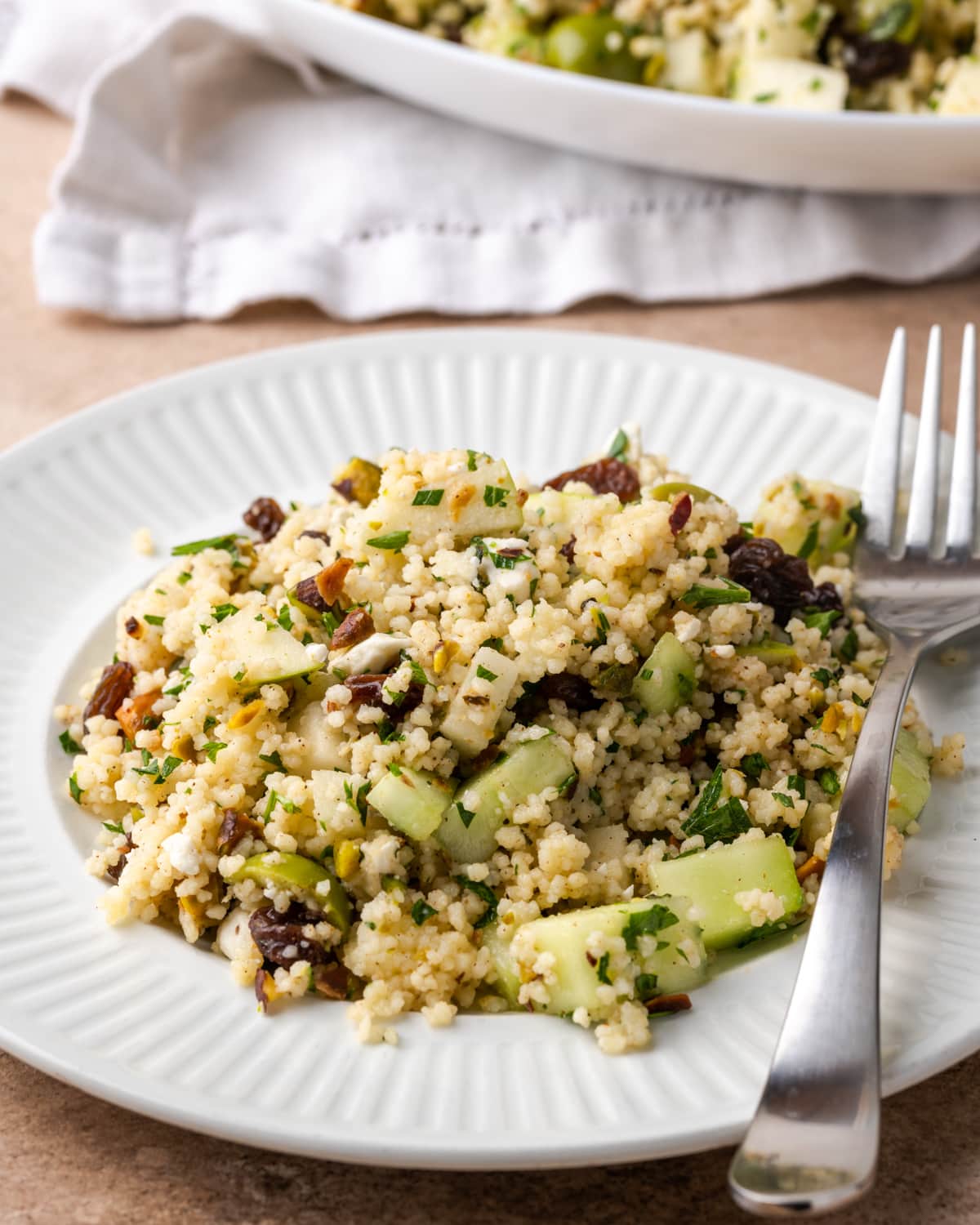 Una porción de ensalada mediterránea de cuscús en un plato blanco con un tenedor.