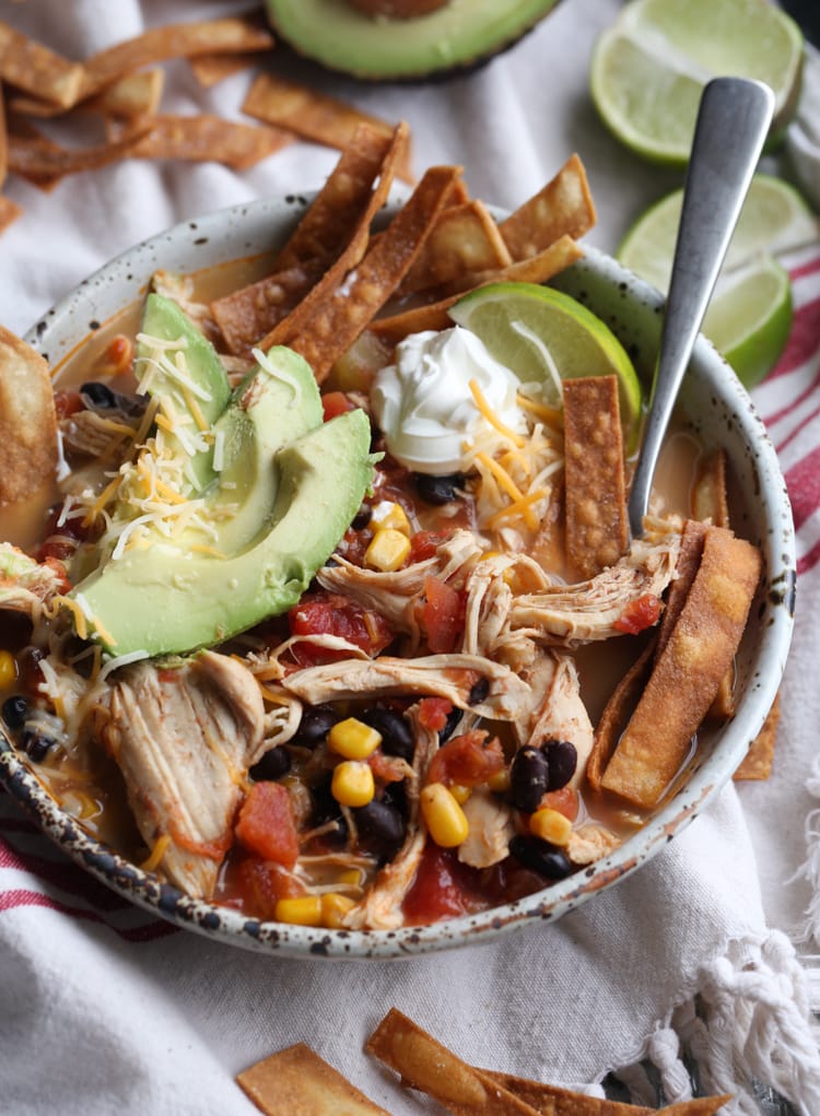 Sopa de tortilla de pollo adornada con aguacate, papas fritas, crema agria y lima