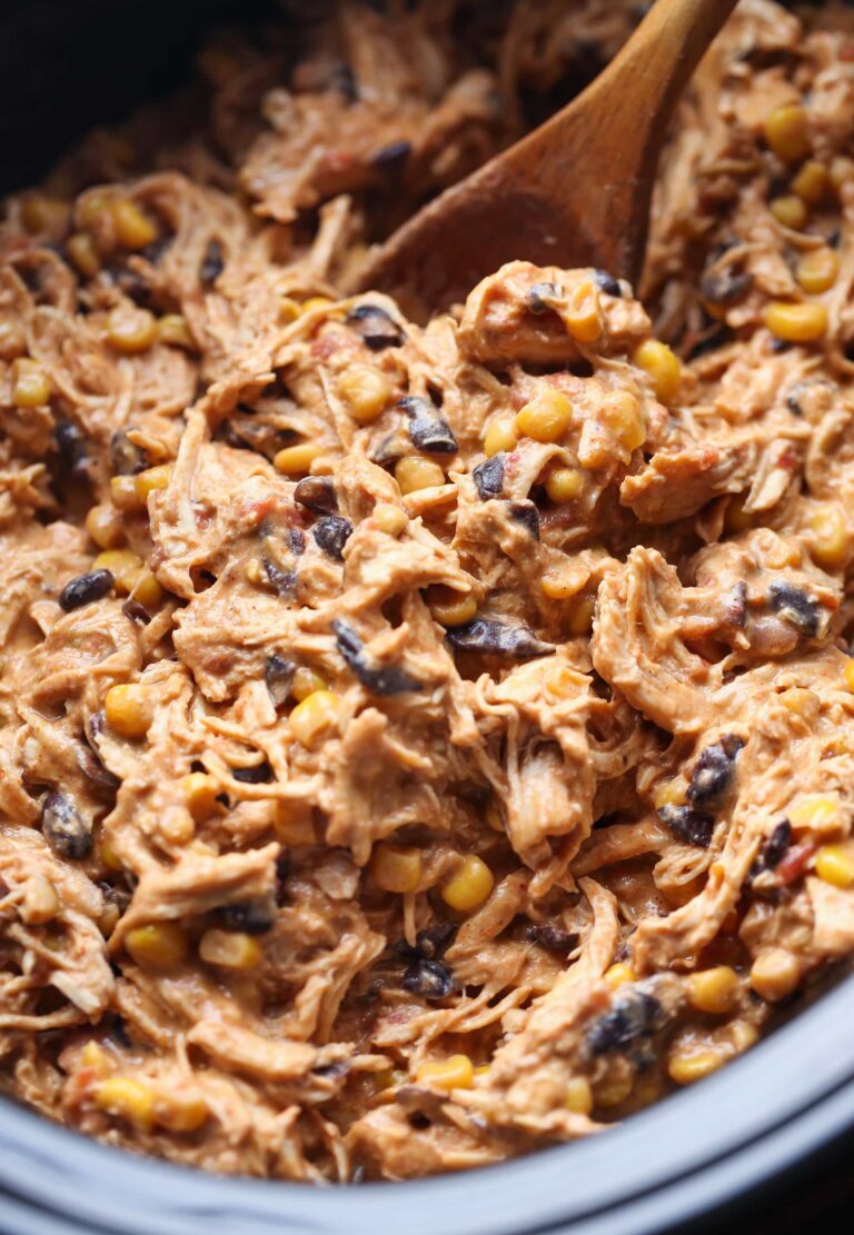 Una olla de cocción lenta llena de cremoso pollo fiesta revuelto con una cuchara de madera