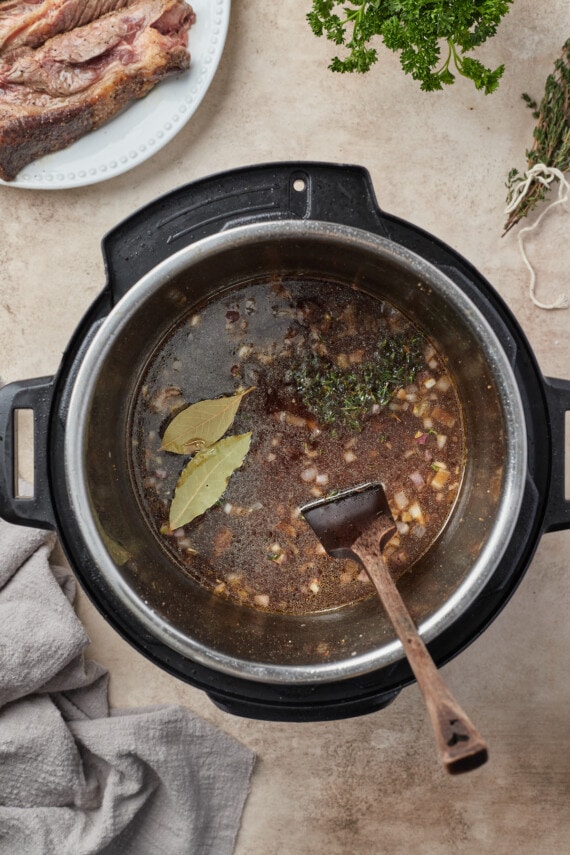Caldo, hierbas, cebollas y ajo combinados en una olla instantánea.