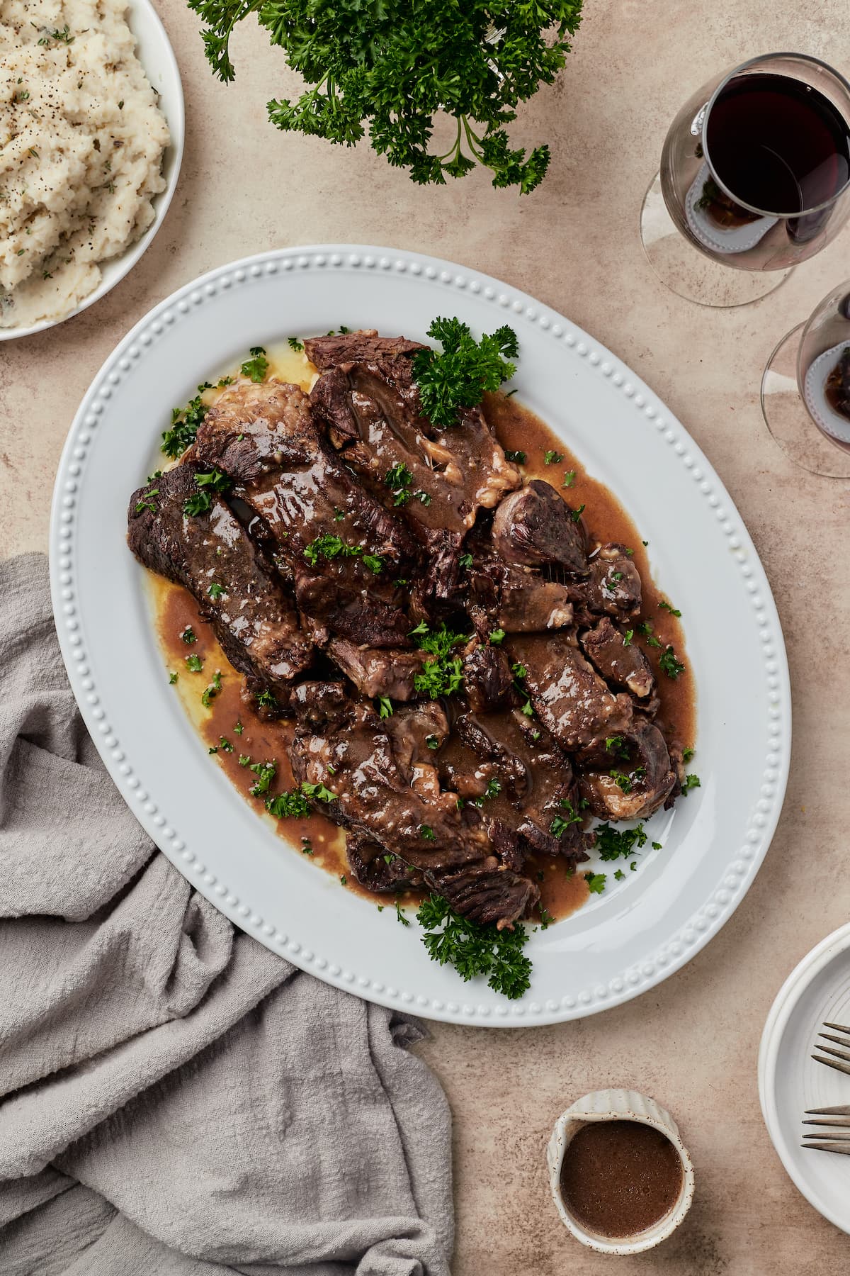 Una mesa con jugosas costillas de res cubiertas con salsa de vino tinto en un plato blanco.