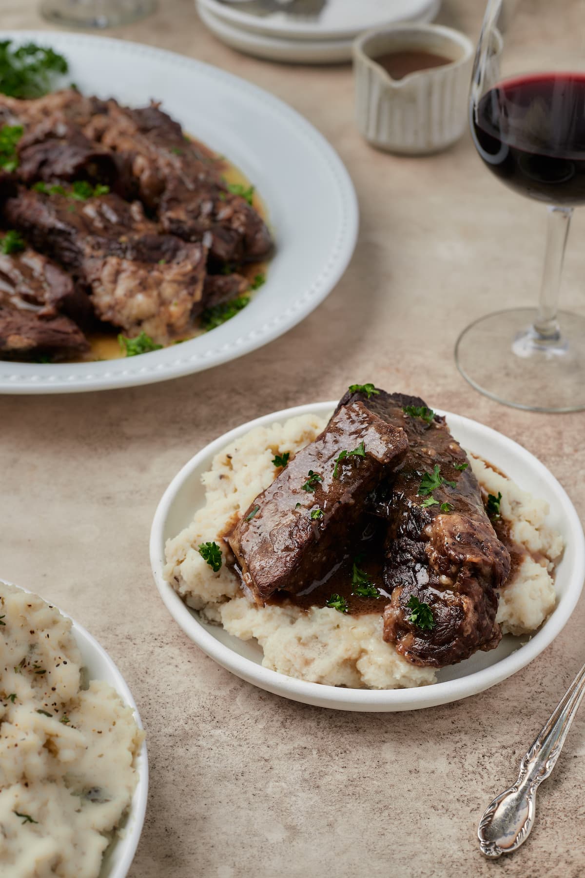 Costillas cortas Instant Pot servidas en un tazón sobre puré de papas, con un plato de costillas cortas en el fondo.