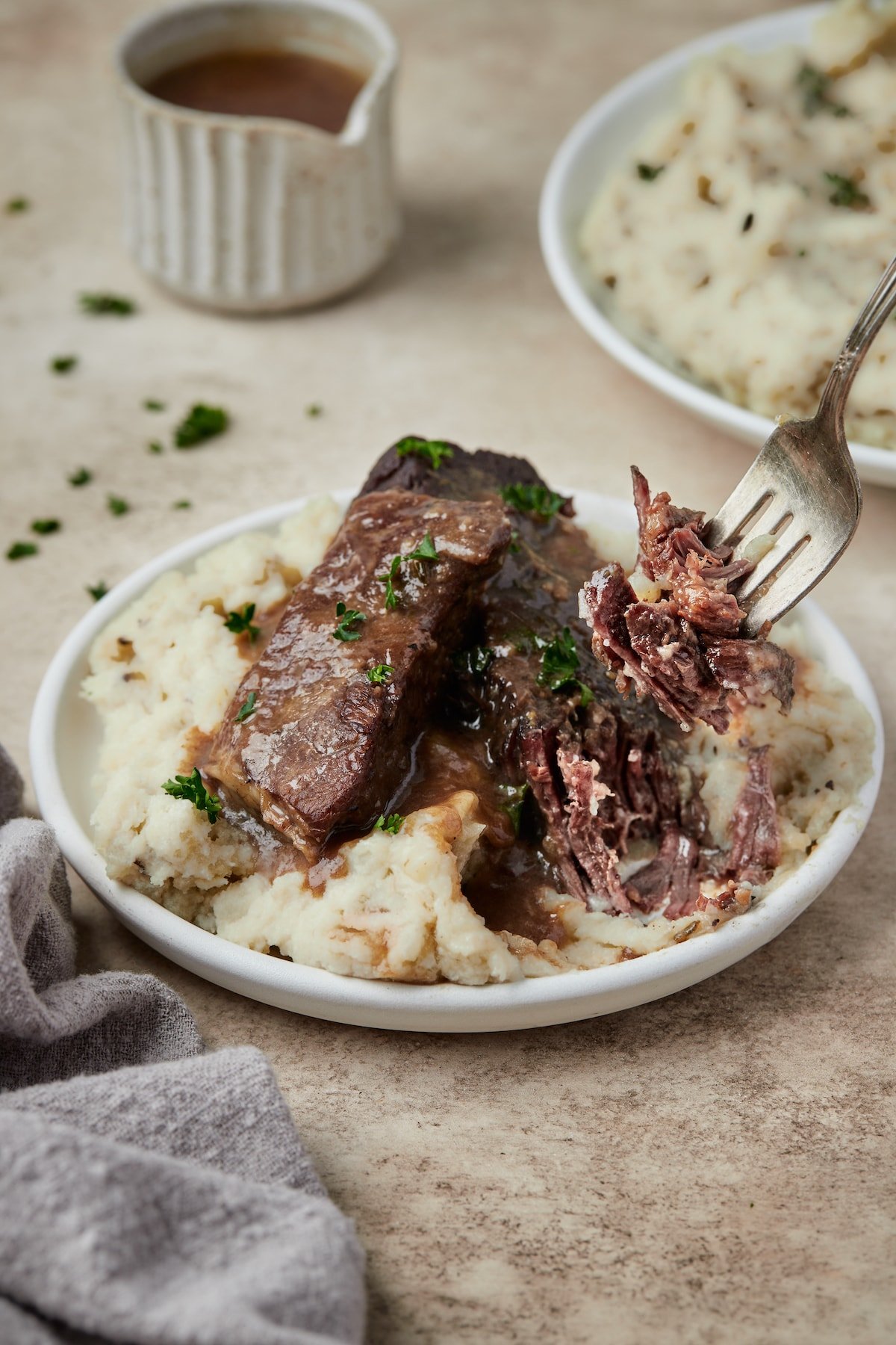 Un tenedor recogiendo una costilla corta Instant Pot servida en un tazón sobre puré de papas.