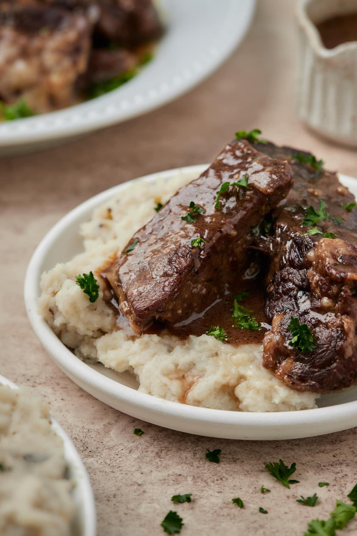 Costillas cortas Instant Pot servidas en un tazón sobre puré de papas, rociadas con salsa de vino tinto.