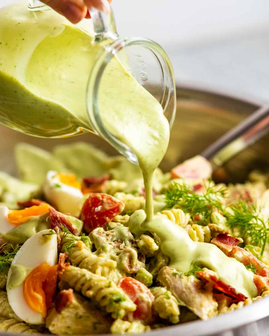 Verter aderezo ranch de aguacate sobre ensalada de pasta con pollo