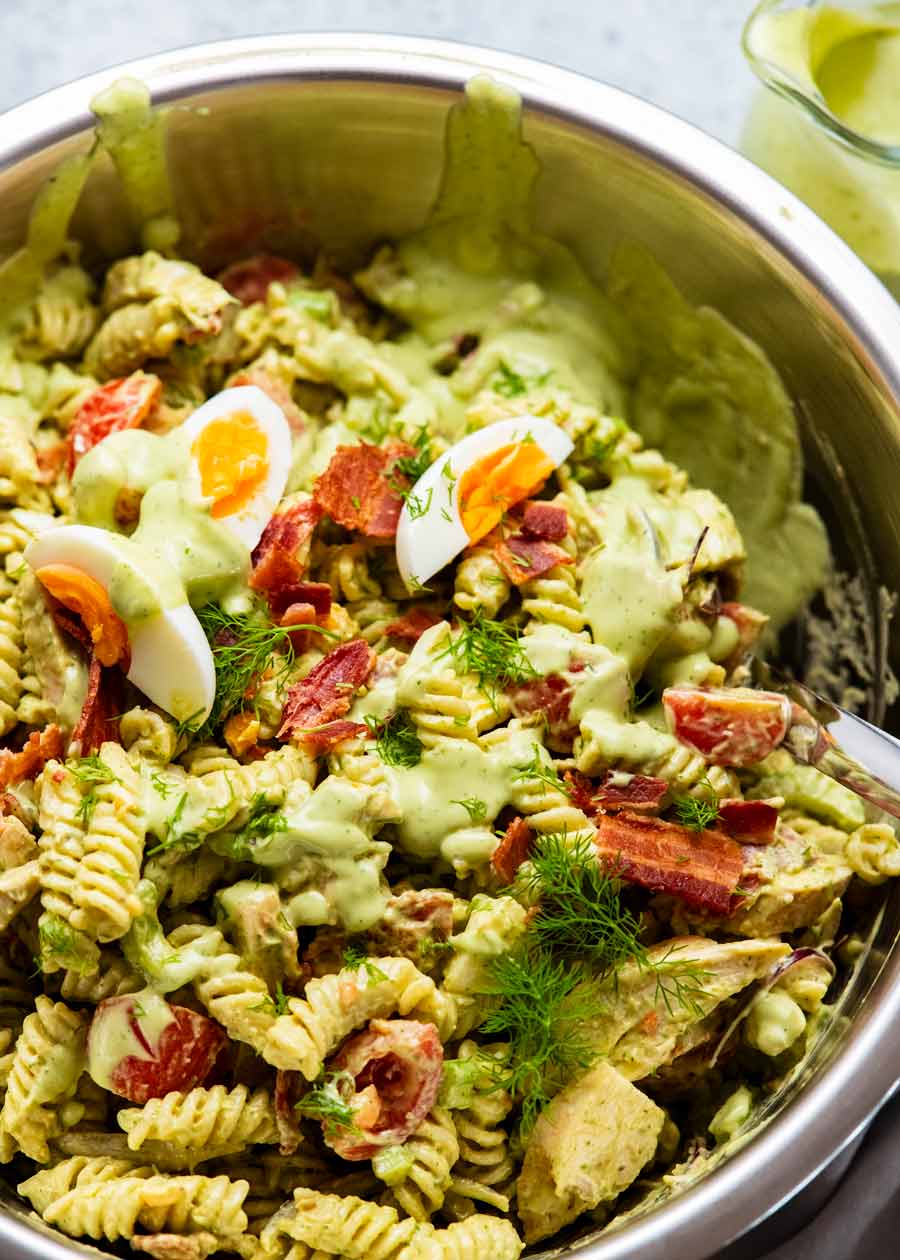 Recipiente grande lleno de ensalada de pasta con aderezo ranch de aguacate