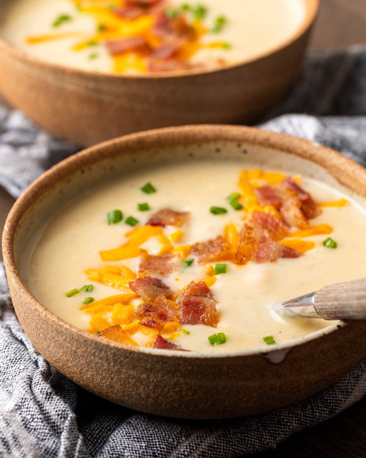 ¡Esta sencilla sopa instantánea de papas está lista en minutos! Una receta de sopa sedosa, cremosa y nutritiva cargada de queso derretido y verduras. Dos tazones uno al lado del otro de sopa de papa Instant Pot cargada cubierta con queso rallado, trocitos de tocino y cebollín.