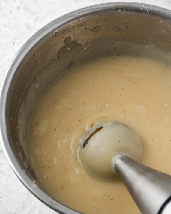 Una licuadora de inmersión hace puré de papas en una olla.